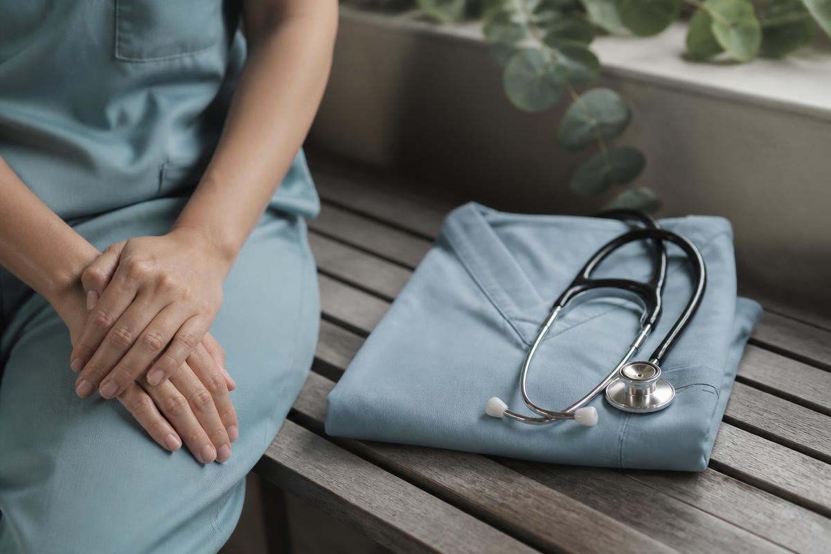 A healthcare worker resting beside folded scrubs and a stethoscope